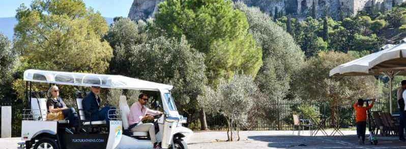 Tourists riding a tuk tuk in athens. Acroplis in the background.